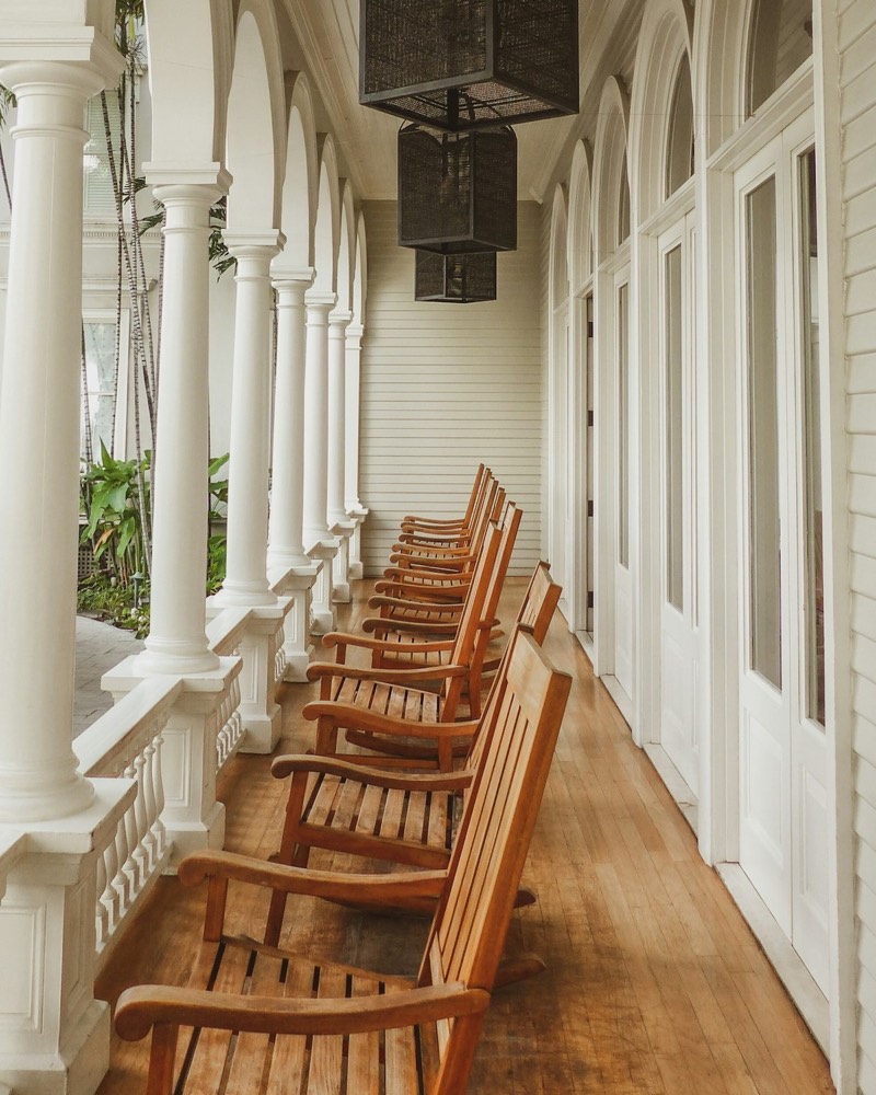 A covered porch lined with wooden rocking chairs between white columns.